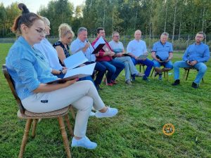 ludzie siedzący na krzesłach w półkręgu, krzesła na trawie, kobieta czyta