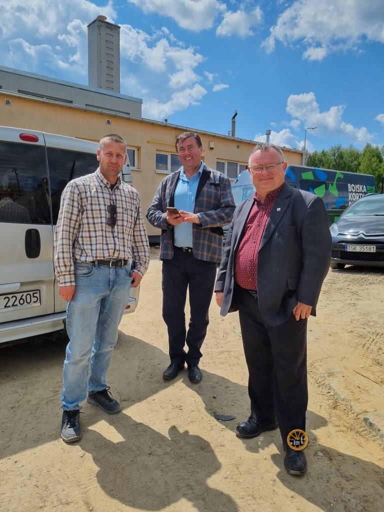 Zdjęcie przedstawia trzech mężczyzn pozujących do zdjęcia w naturalnych pozach, są uśmiechnięci, z tyłu budynek szkoły, słoneczny dzień