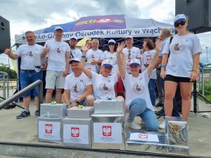 Na zdjęciu znajduje się grupa laureatów turnieju sołtysa. Ubrani są w białe koszulki startowe i czapeczki, cześć z nich ma podniesione ręce, z tyłu widać namiot ośrodka kultury w Wąchocku