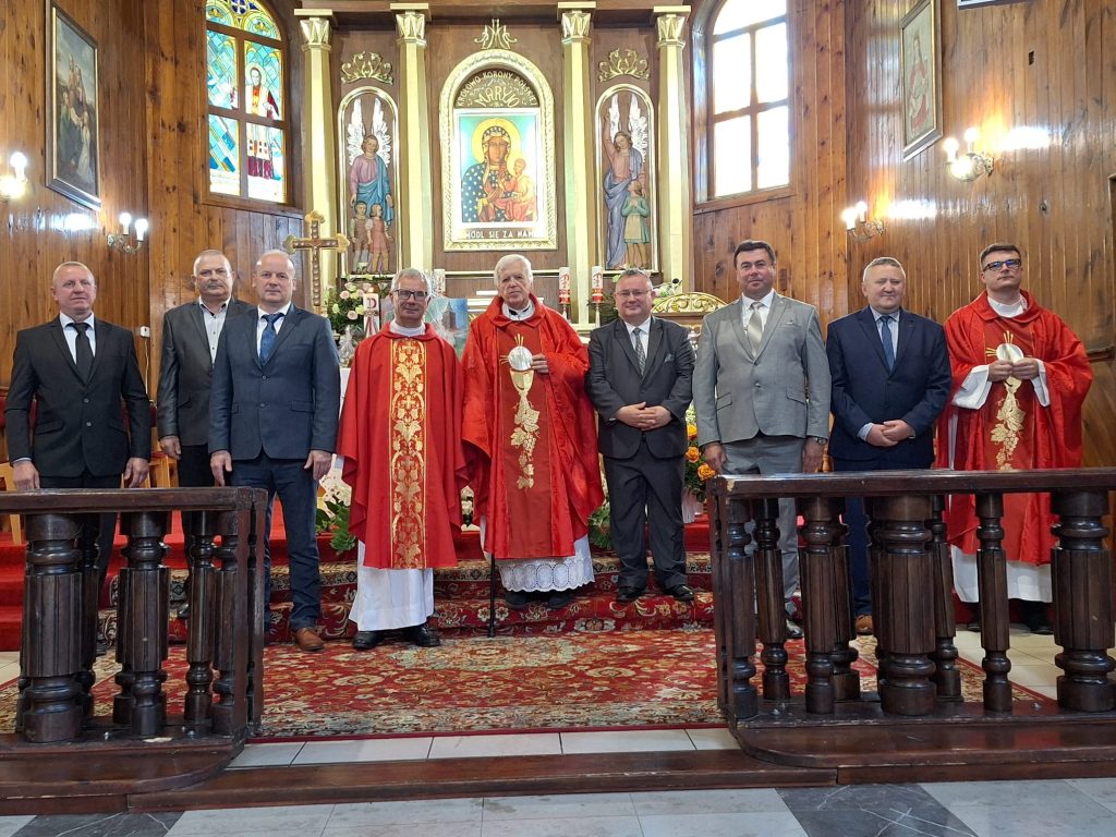 Zdjęcie przedstawia ustawionych przed ołtarzem mężczyzn: trzech księży ubranych z czerwone szaty oraz trzech w garniturach