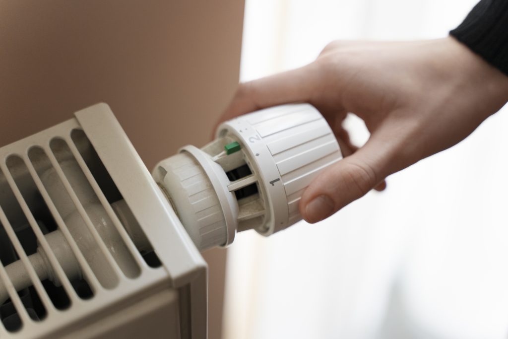Damska dłoń na pokrętle od regulacji temperatury przy kaloryferze