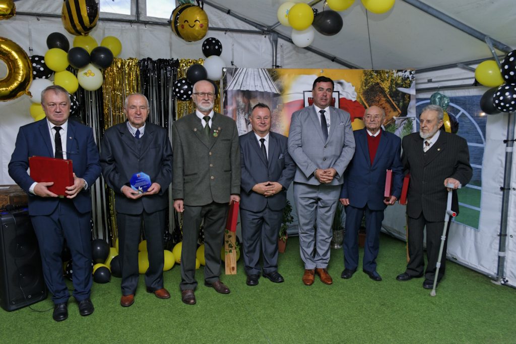 Siedmiu mężczyzn ubranych formalnie pozuje razem w świątecznym namiocie udekorowanym czarnymi i żółtymi balonami z okazji specjalnej okazji.
