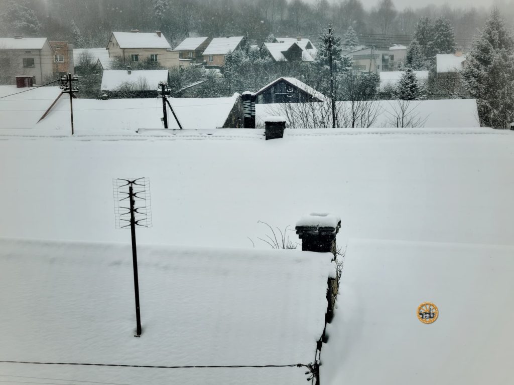 Śnieżny krajobraz z pokrytymi dachami i liniami energetycznymi tworzy spokojną, zimową scenerię na terenie dzielnicy mieszkalnej.