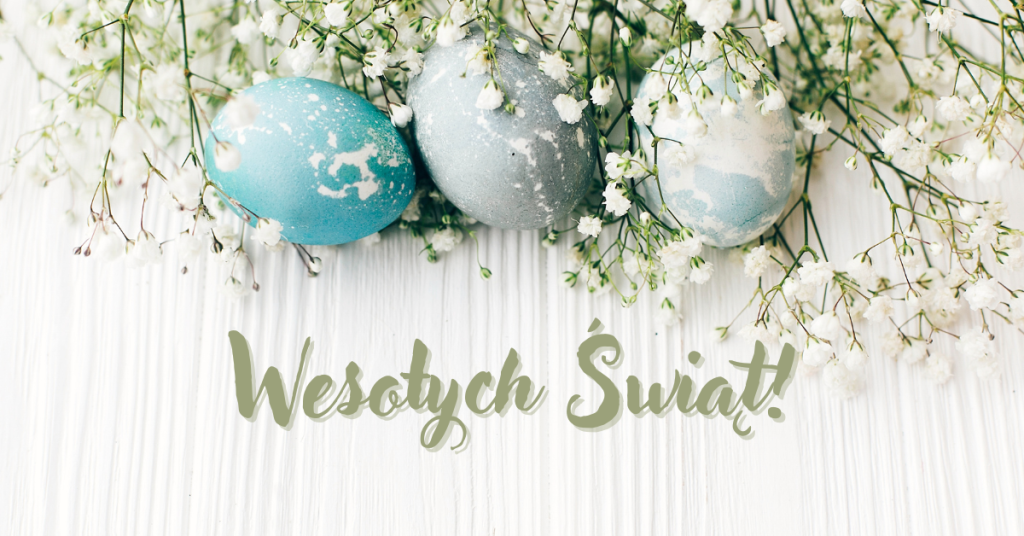 Grafika wielkanocna przedstawiająca trzy pisanki w odcieniach błękitu i szarości, ułożone na białym drewnianym tle wśród drobnych, białych kwiatuszków gipsówki. W dolnej części zdjęcia znajduje się ozdobny napis w kolorze szałwiowej zieleni: „Wesołych Świąt!”.